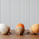 Decorative rope and paper acorns in cream, orange and yellow, styled in an autumn display with pumpkins and seasonal foliage.