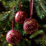 Berry red and gold papier-mâché Christmas baubles with hand-painted sprigs and velvet ribbons