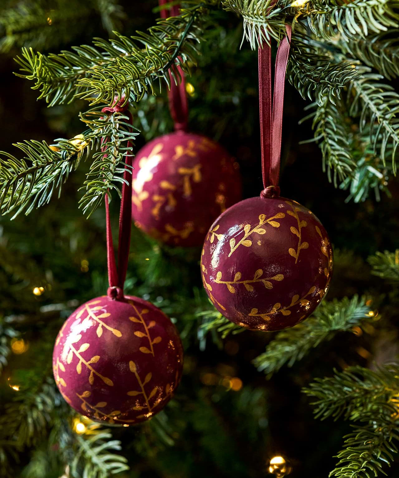 Berry red and gold papier-mâché Christmas baubles with hand-painted sprigs and velvet ribbons