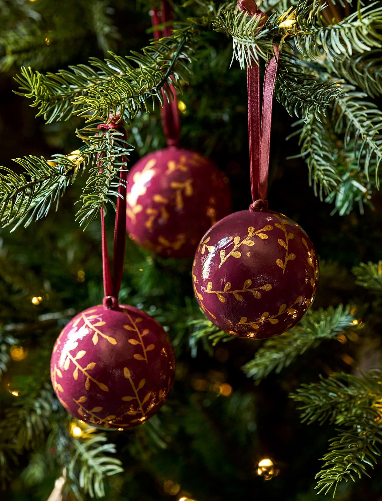 Berry red and gold papier-mâché Christmas baubles with hand-painted sprigs and velvet ribbons