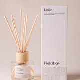 FieldDay Linen reed diffuser with flax, lavender and rosemary fragrance in a glass bottle with wooden cap and natural reeds.