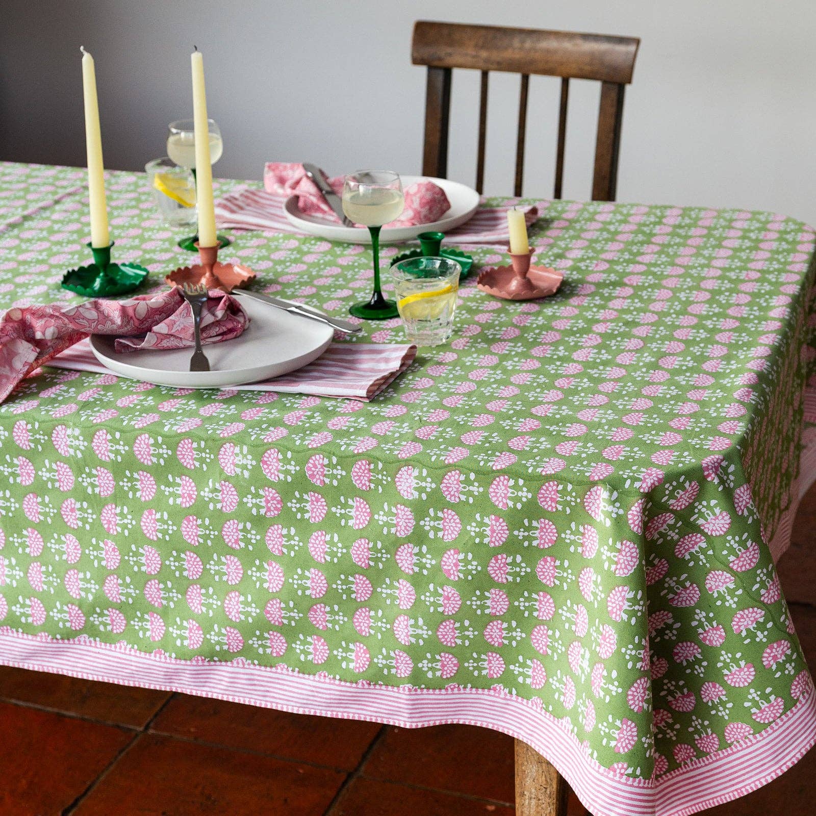 Green hand block printed cotton tablecloth with pink fan motifs and striped border styled on an elegant dining table.