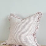 Hallie pink stripe stonewashed linen cushion with ruffled edging and feather filling, styled on a sofa to add relaxed country charm and soft texture to a living room.