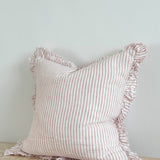 Hallie pink stripe stonewashed linen cushion with ruffled edging and feather filling, styled on a sofa to add relaxed country charm and soft texture to a living room.