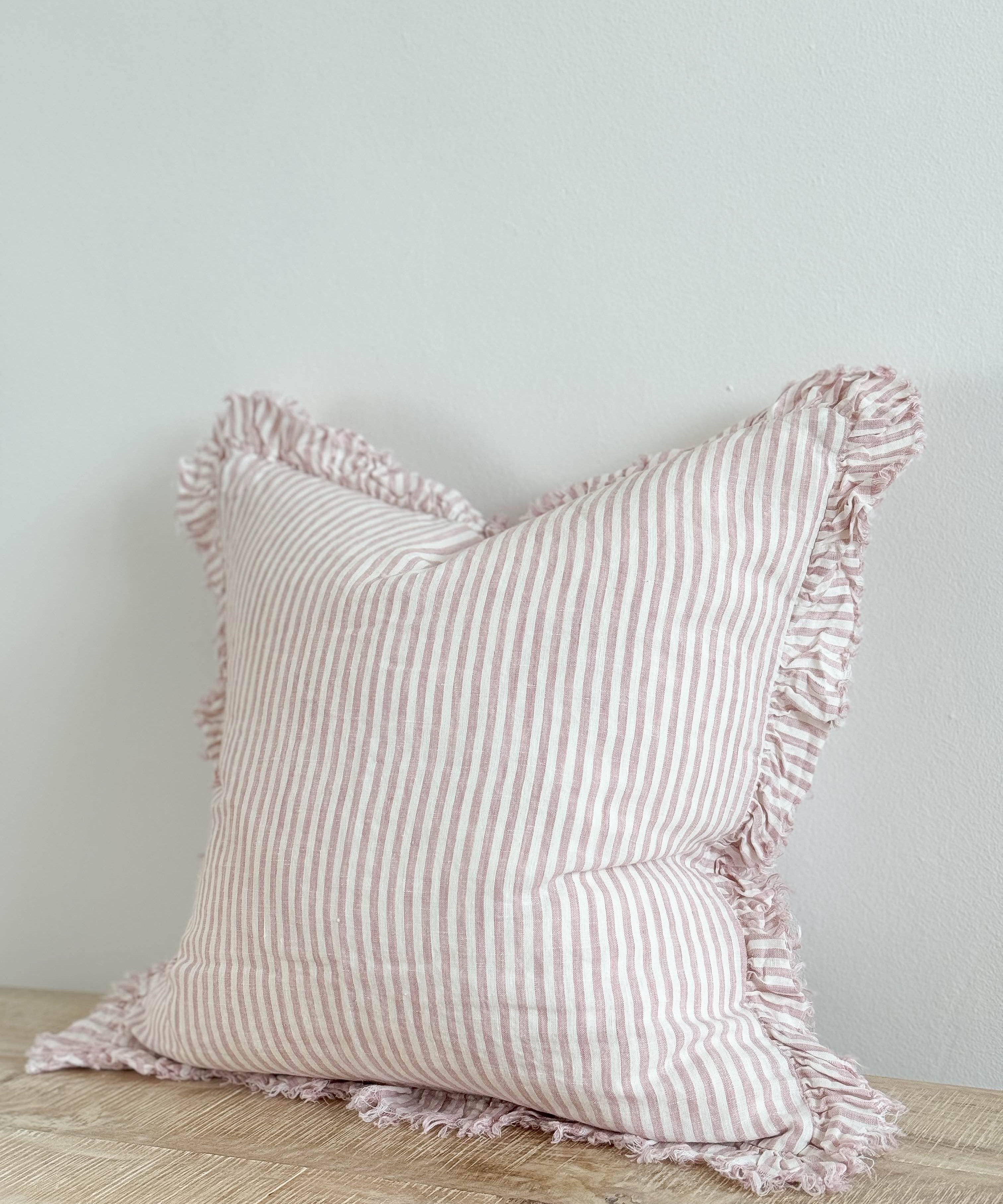 Hallie pink stripe stonewashed linen cushion with ruffled edging and feather filling, styled on a sofa to add relaxed country charm and soft texture to a living room.