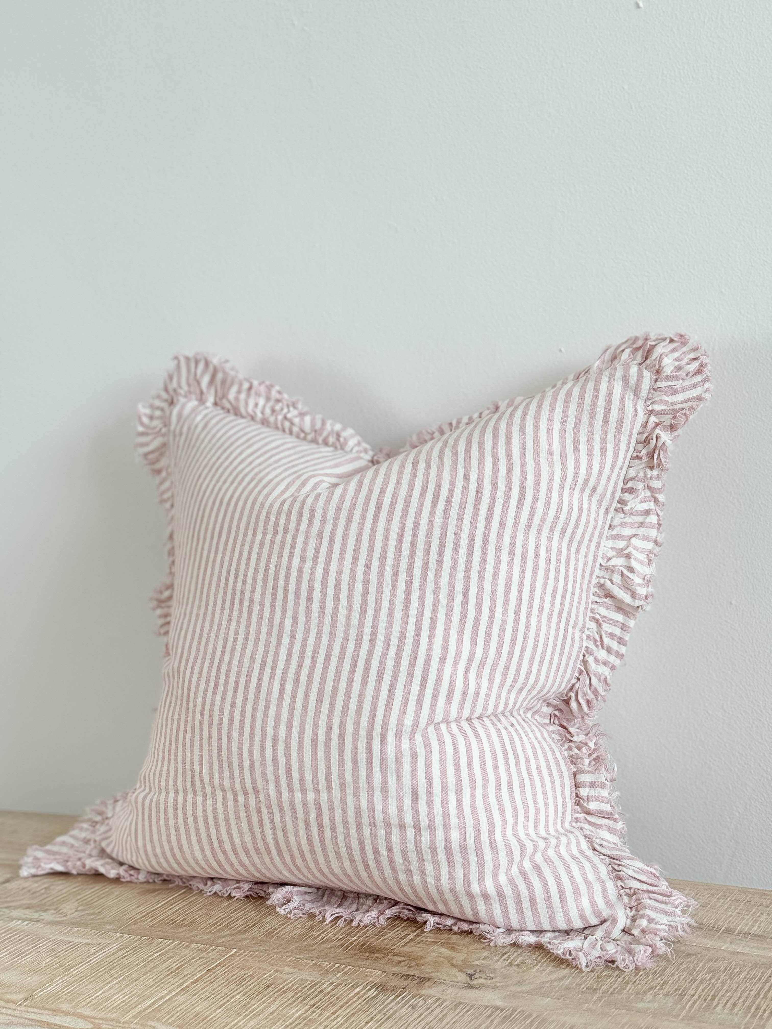 Hallie pink stripe stonewashed linen cushion with ruffled edging and feather filling, styled on a sofa to add relaxed country charm and soft texture to a living room.