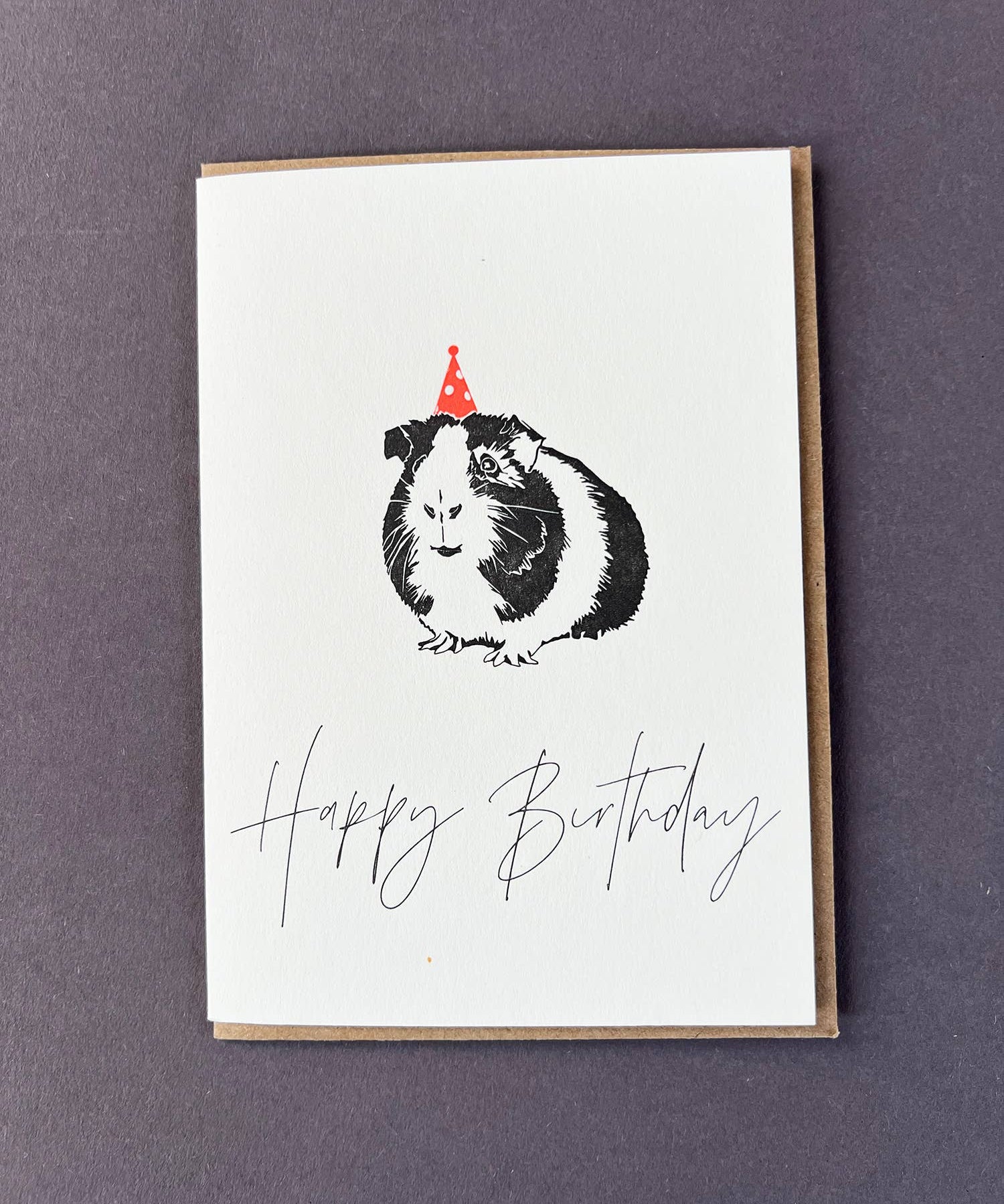 Happy Birthday letterpress greetings card featuring a cute guinea pig wearing a neon spotty party hat, designed by Penguin Ink.