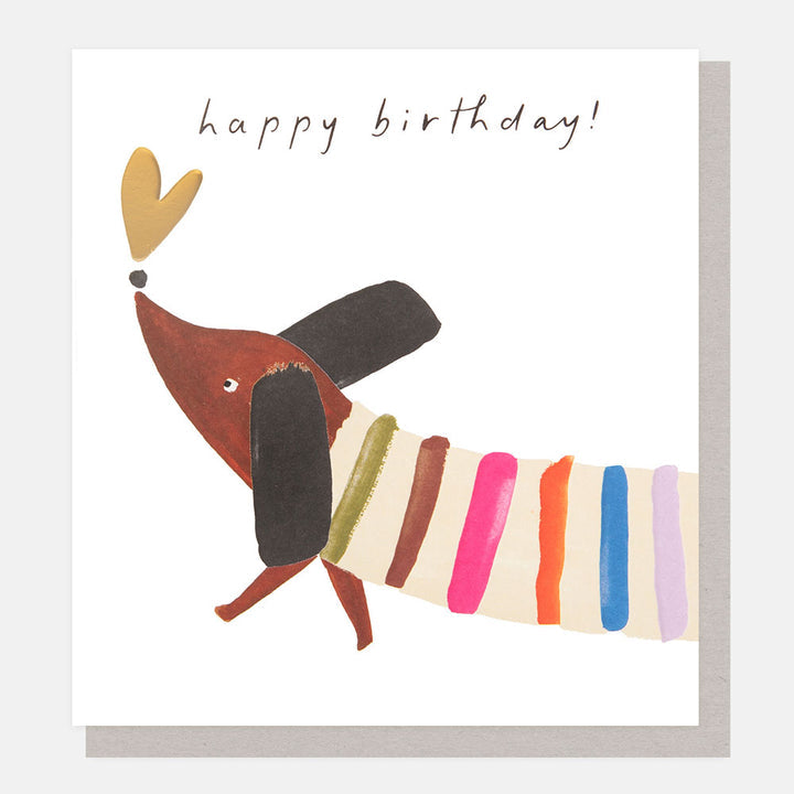 Happy Birthday greetings card featuring a cute sausage dog wearing a colourful striped jumper with gold foil and embossed detailing.