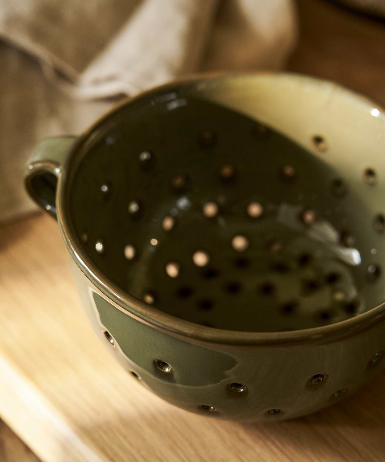 Ithaca Moss green stoneware berry bowl and colander with perforated sides, organic shape and practical handles.