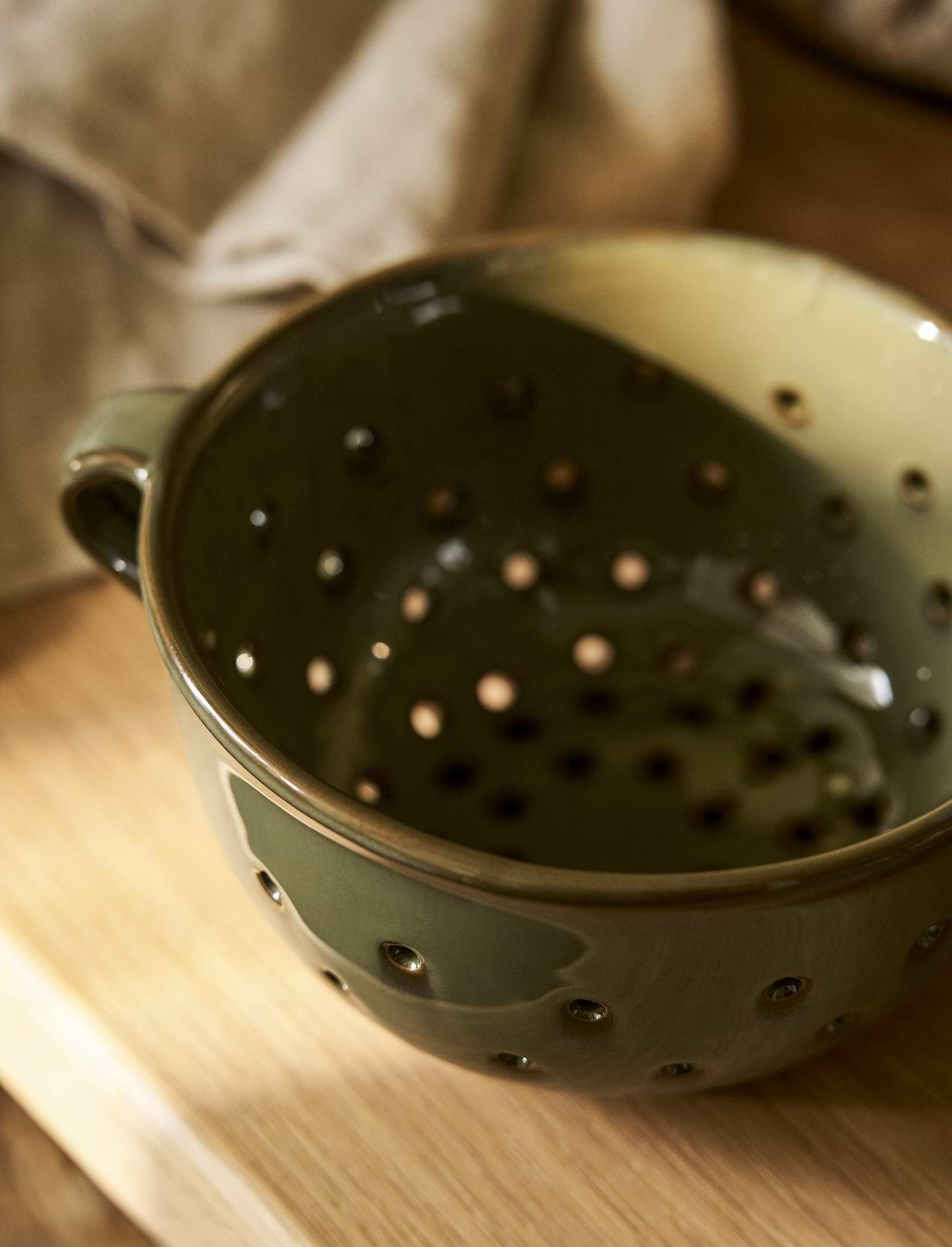 Ithaca Moss green stoneware berry bowl and colander with perforated sides, organic shape and practical handles.