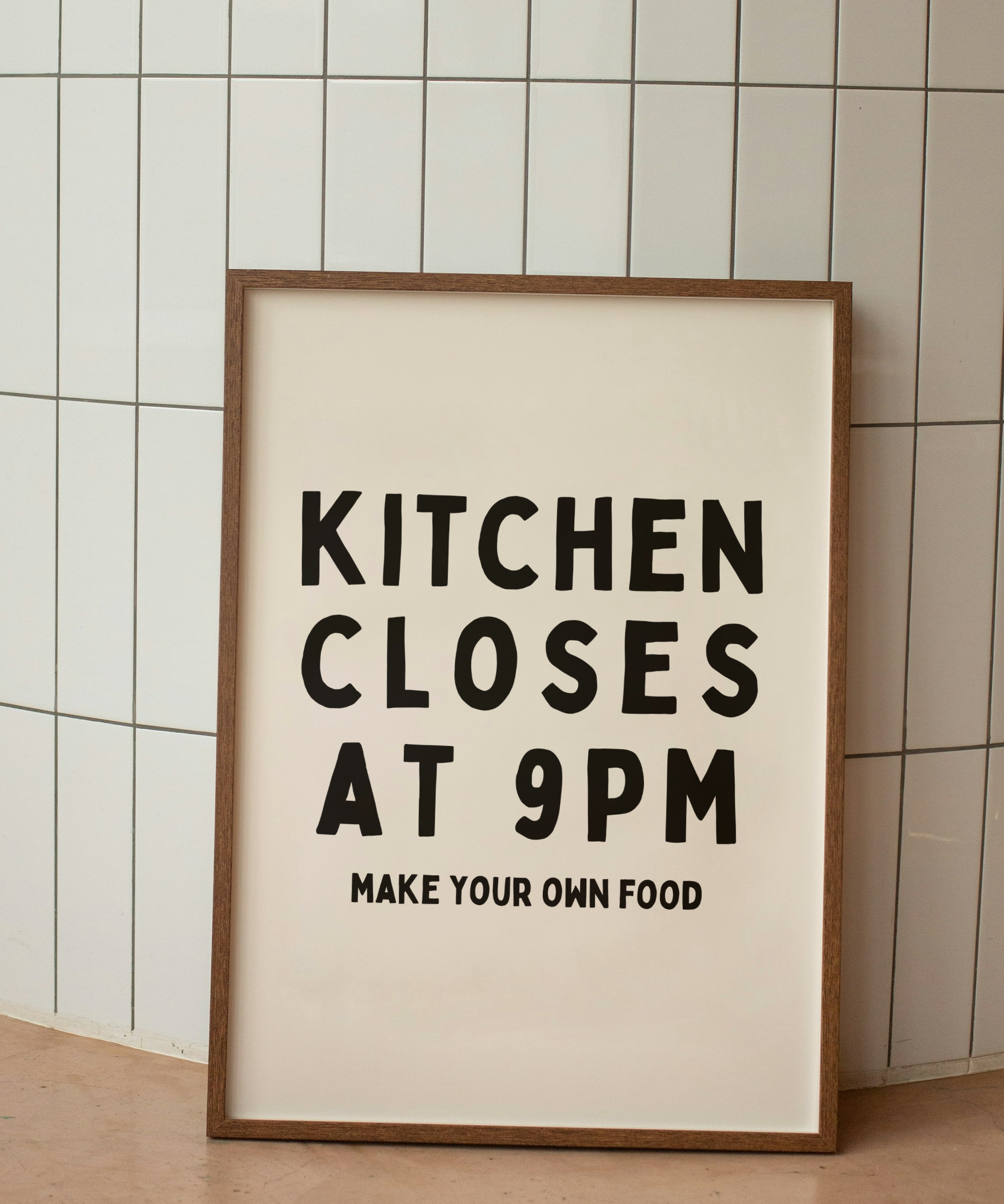 Framed poster with text 'Kitchen Closes at 9PM Make Your Own Food' against a tiled wall.