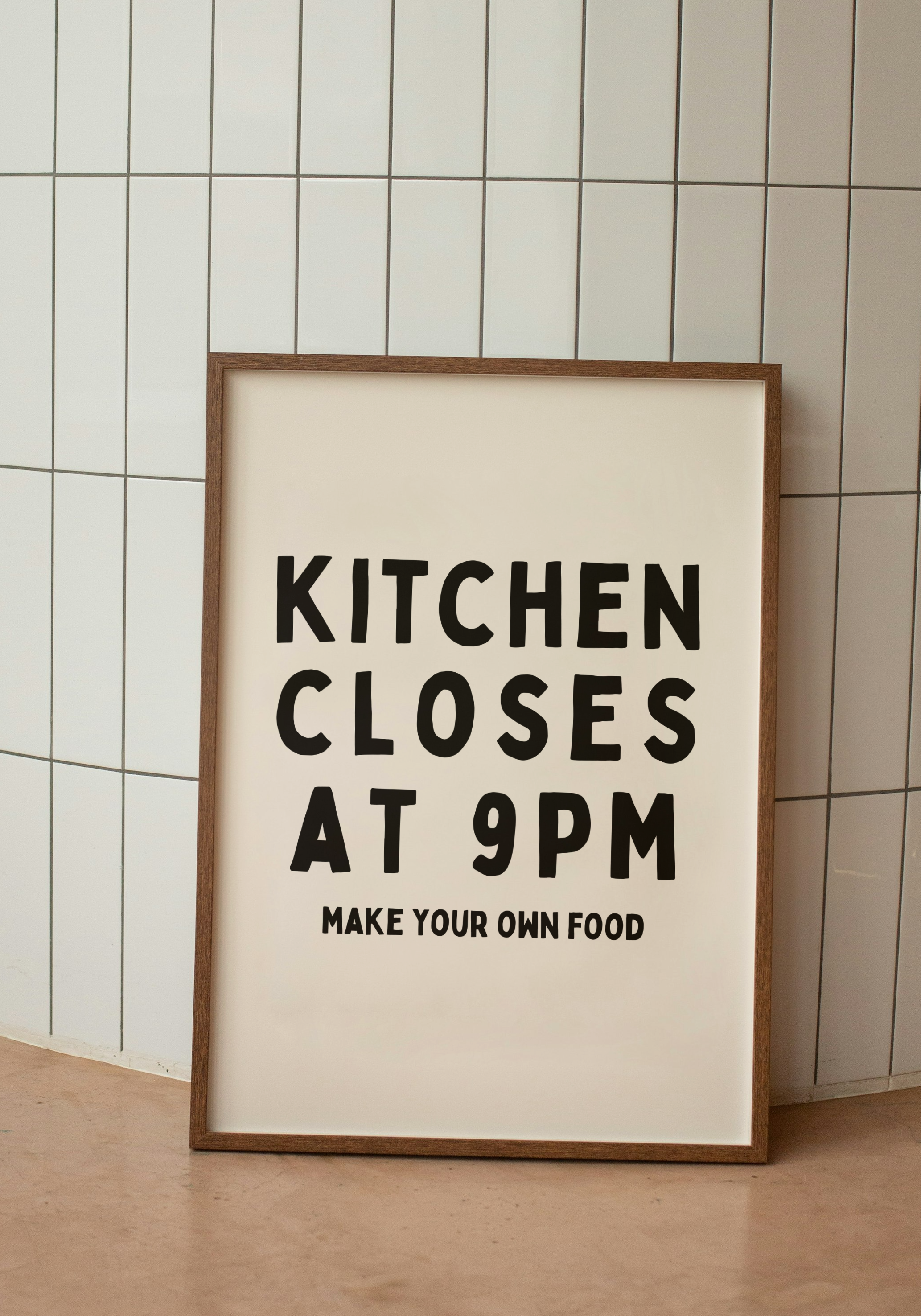 Framed poster with text 'Kitchen Closes at 9PM Make Your Own Food' against a tiled wall.