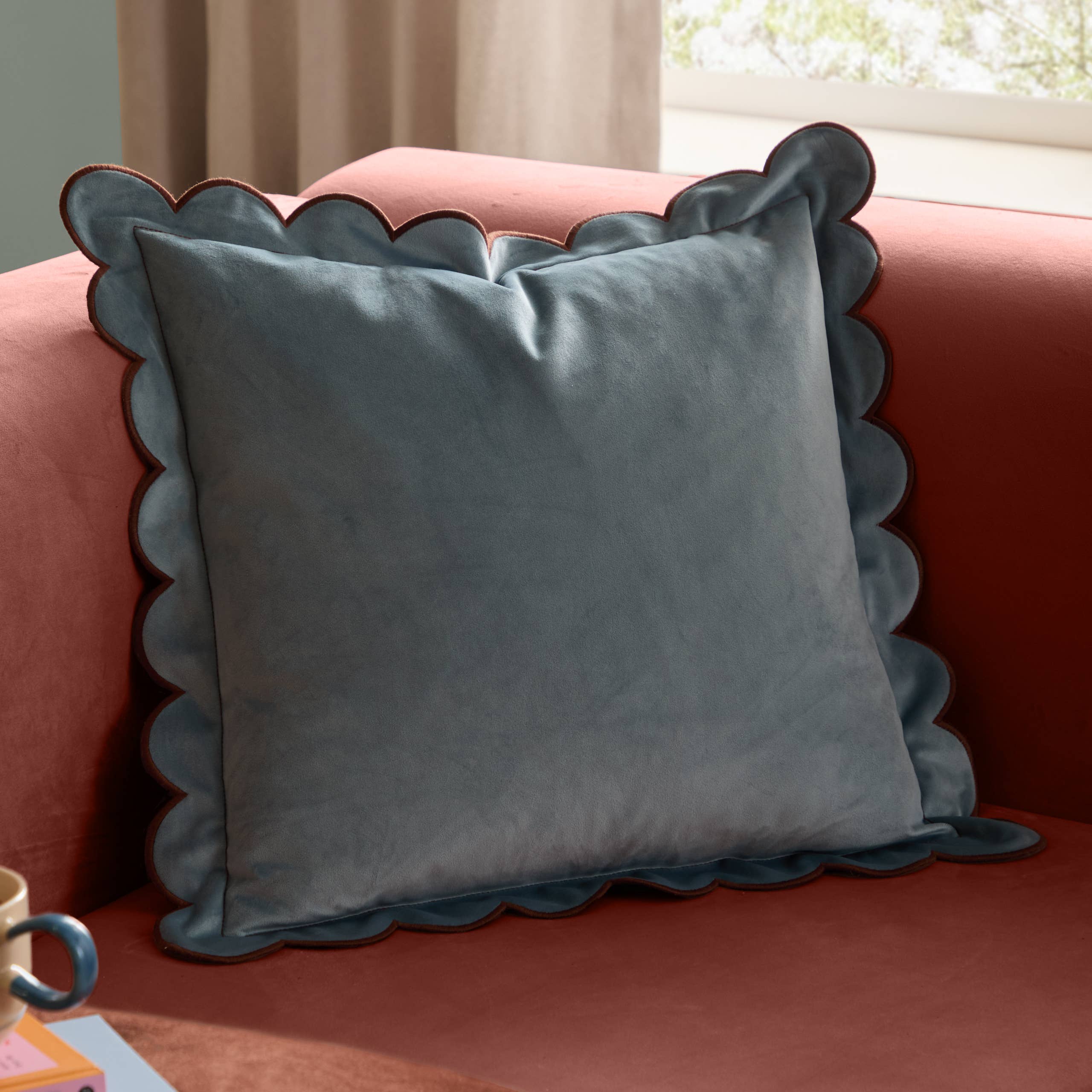 Lil Scallop velvet cushion in blue and brown with a soft velvet finish, scalloped edge and contrast trim, styled on a contemporary sofa.