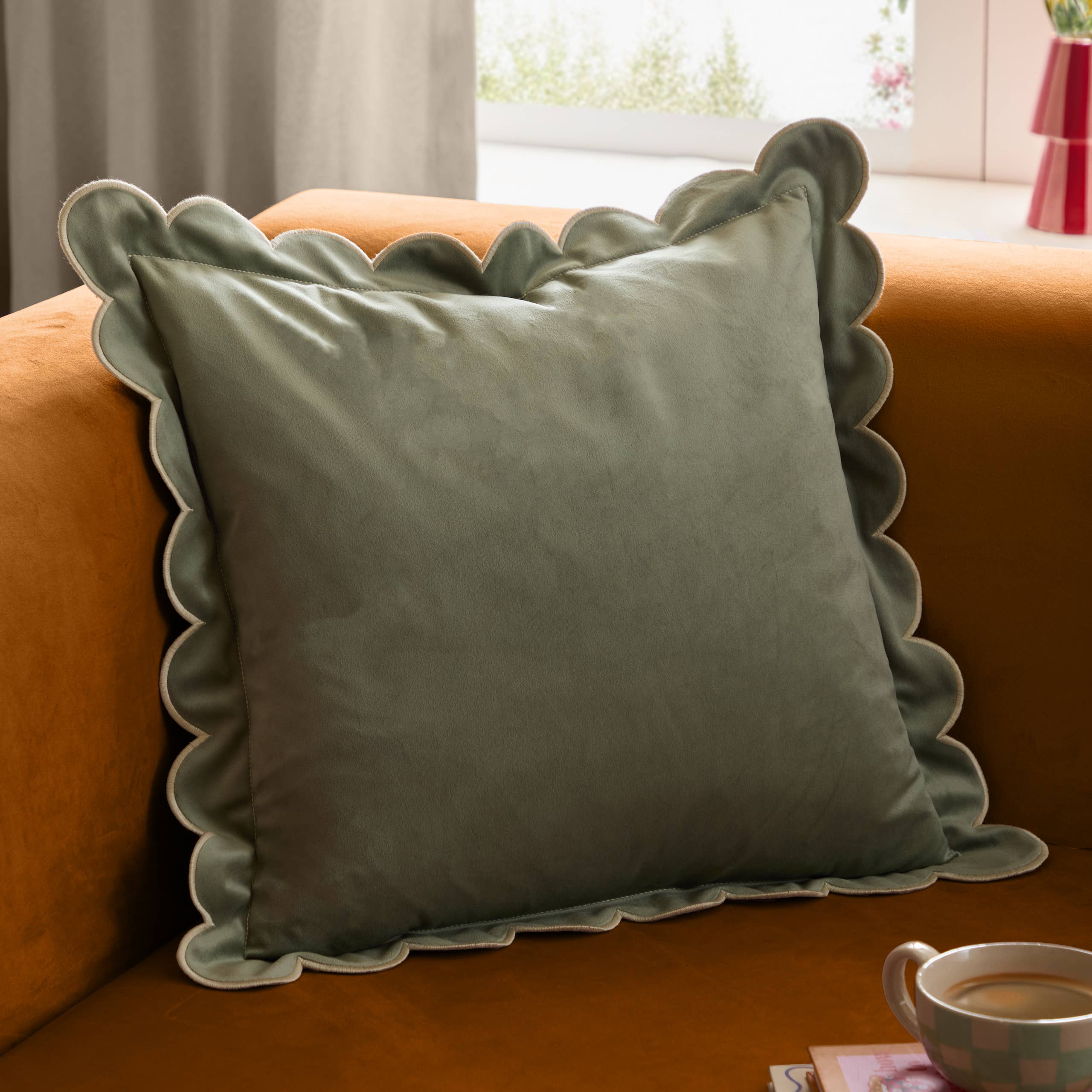 Lil Scallop velvet cushion in green and natural with a soft velvet finish, scalloped edge and contrast trim, styled on a contemporary sofa.