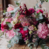 A luxurious floral arrangement featuring a marshmallow pink and rich marsala red colour palette, with a variety of flowers including roses, hydrangeas, snapdragons, lisianthus, and seasonal foliage