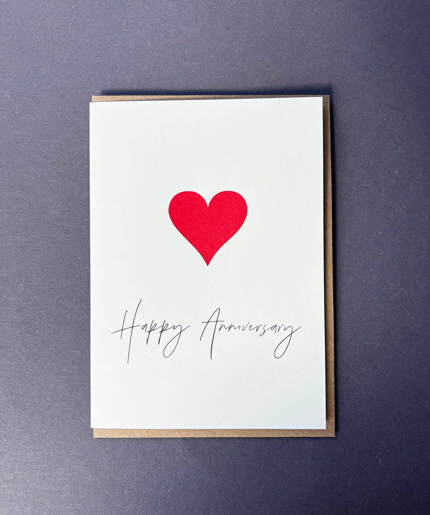 Penguin Ink Happy Anniversary Heart letterpress card featuring a red heart and elegant anniversary calligraphy, printed on 100% recycled board with a tactile embossed finish.