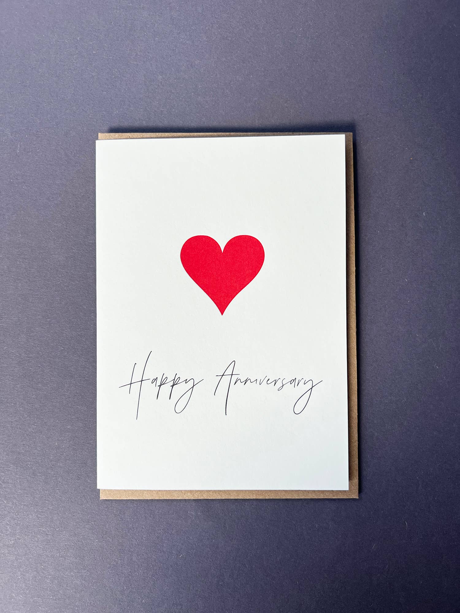 Penguin Ink Happy Anniversary Heart letterpress card featuring a red heart and elegant anniversary calligraphy, printed on 100% recycled board with a tactile embossed finish.