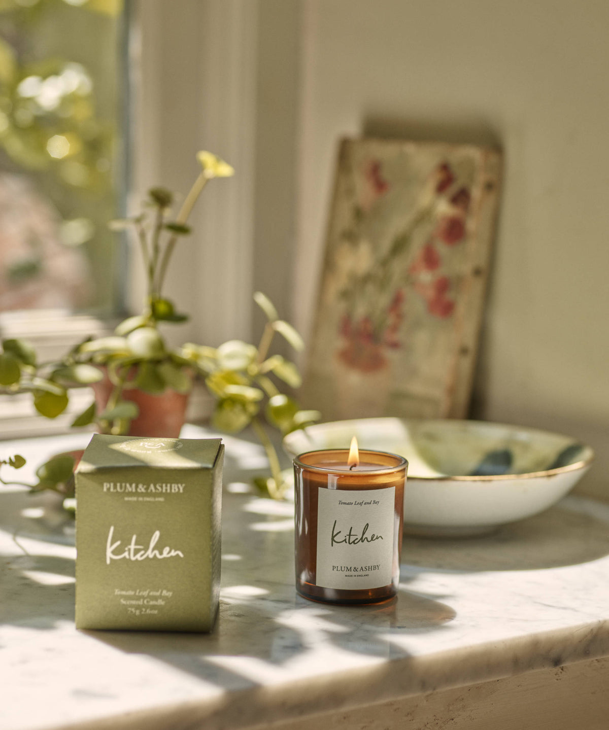 Plum & Ashby 'Kitchen' candle and packaging on a marble surface with plants and a bowl in the background.