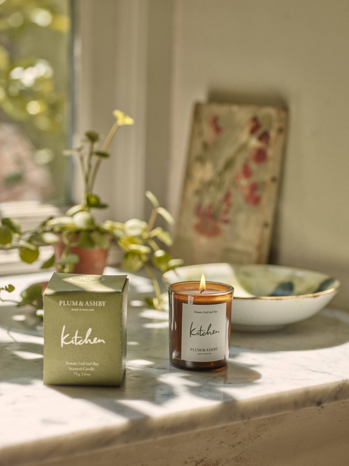 Plum & Ashby 'Kitchen' candle and packaging on a marble surface with plants and a bowl in the background.