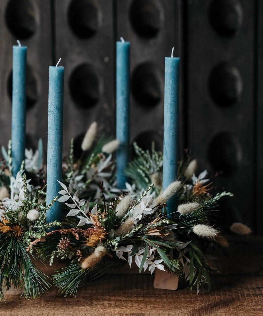 The December Light Christmas Advent wreath with four glacial-blue candles, winter foliage, berries, pine cones and dried botanicals.