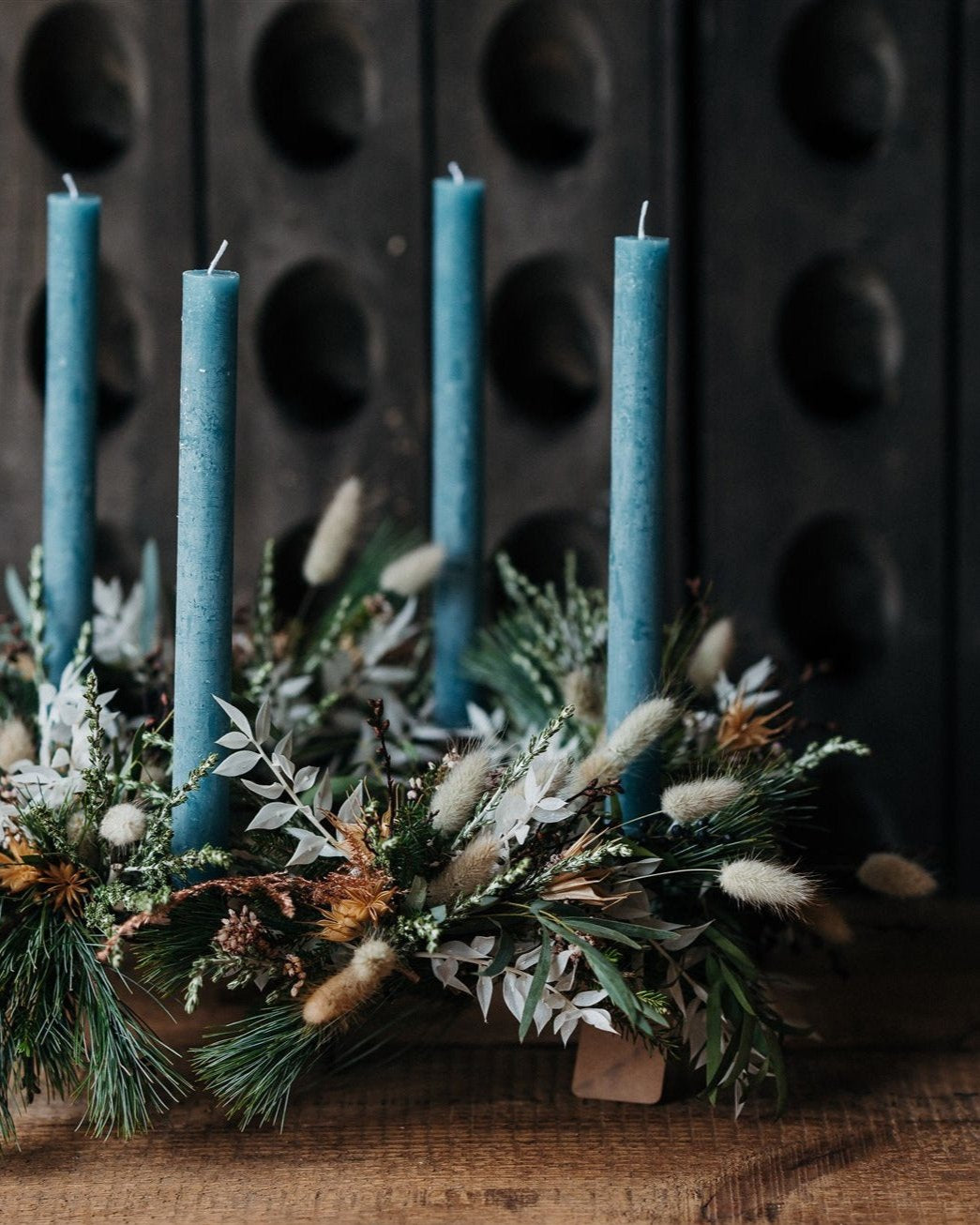 The December Light Christmas Advent wreath with four glacial-blue candles, winter foliage, berries, pine cones and dried botanicals.