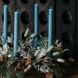 The December Light Christmas Advent wreath with four glacial-blue candles, winter foliage, berries, pine cones and dried botanicals.