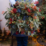 The Merry Berry fresh Christmas door wreath with red Skimmia, rosehips, blue Eryngium, pinecones, winter foliage and velvet ribbon.