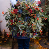 The Merry Berry fresh Christmas door wreath with red Skimmia, rosehips, blue Eryngium, pinecones, winter foliage and velvet ribbon.