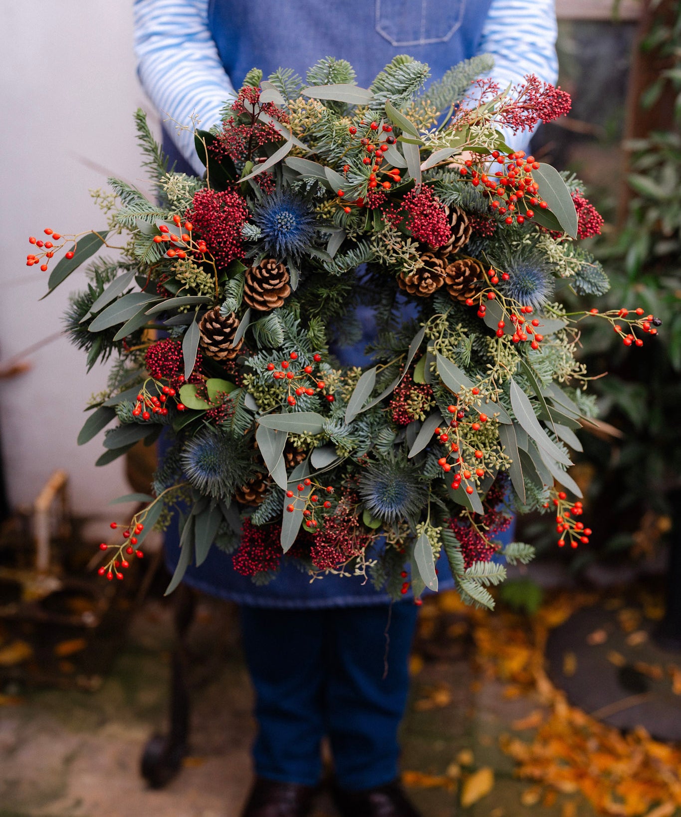 The Merry Berry fresh Christmas door wreath with red Skimmia, rosehips, blue Eryngium, pinecones, winter foliage and velvet ribbon.