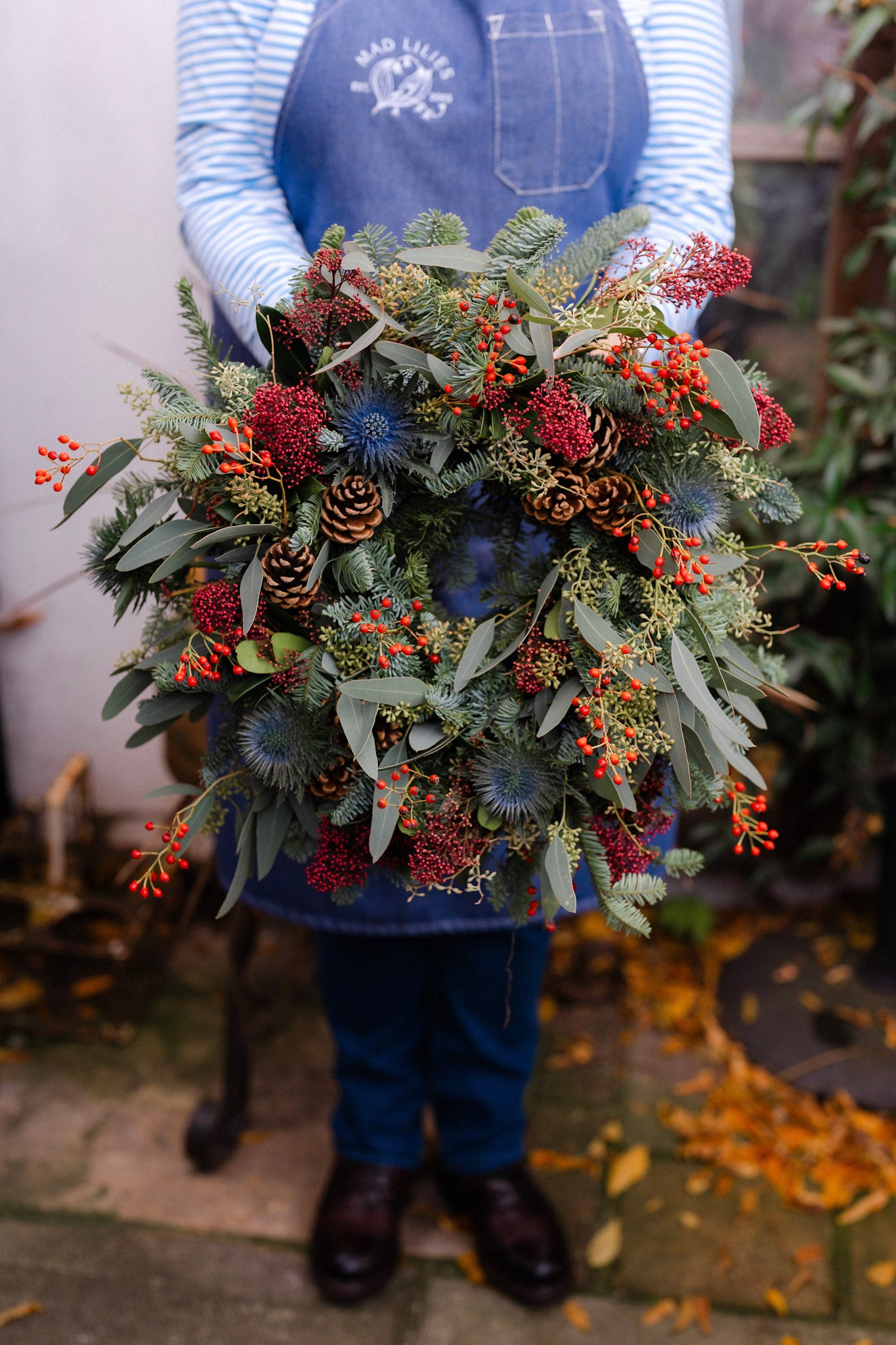 The Merry Berry fresh Christmas door wreath with red Skimmia, rosehips, blue Eryngium, pinecones, winter foliage and velvet ribbon.