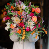 The Pink Bonfire autumn flower bouquet featuring orange Avignon blooms, apricot Miss Piggy roses, vibrant hot pink roses, waxflower and seasonal foliage.
