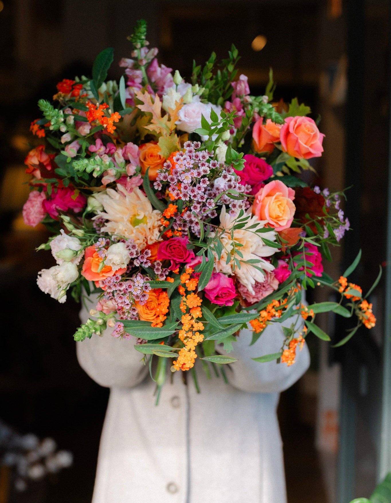 The Pink Bonfire autumn flower bouquet featuring orange Avignon blooms, apricot Miss Piggy roses, vibrant hot pink roses, waxflower and seasonal foliage.