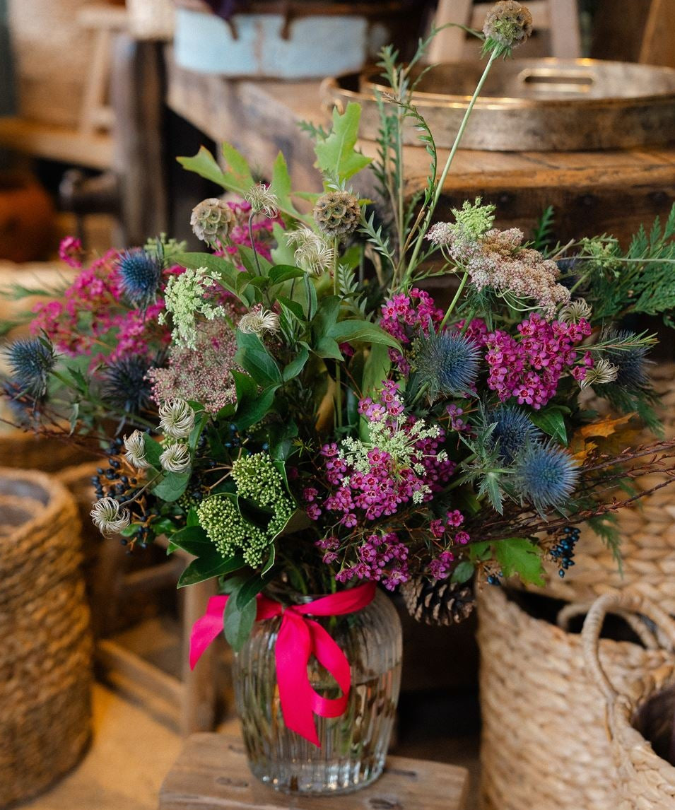 The Wild Revelry, a luxury Christmas hedgerow vase with jewel-toned flowers, thistles and sculptural seedheads. Handcrafted by Mad Lilies in Surrey.