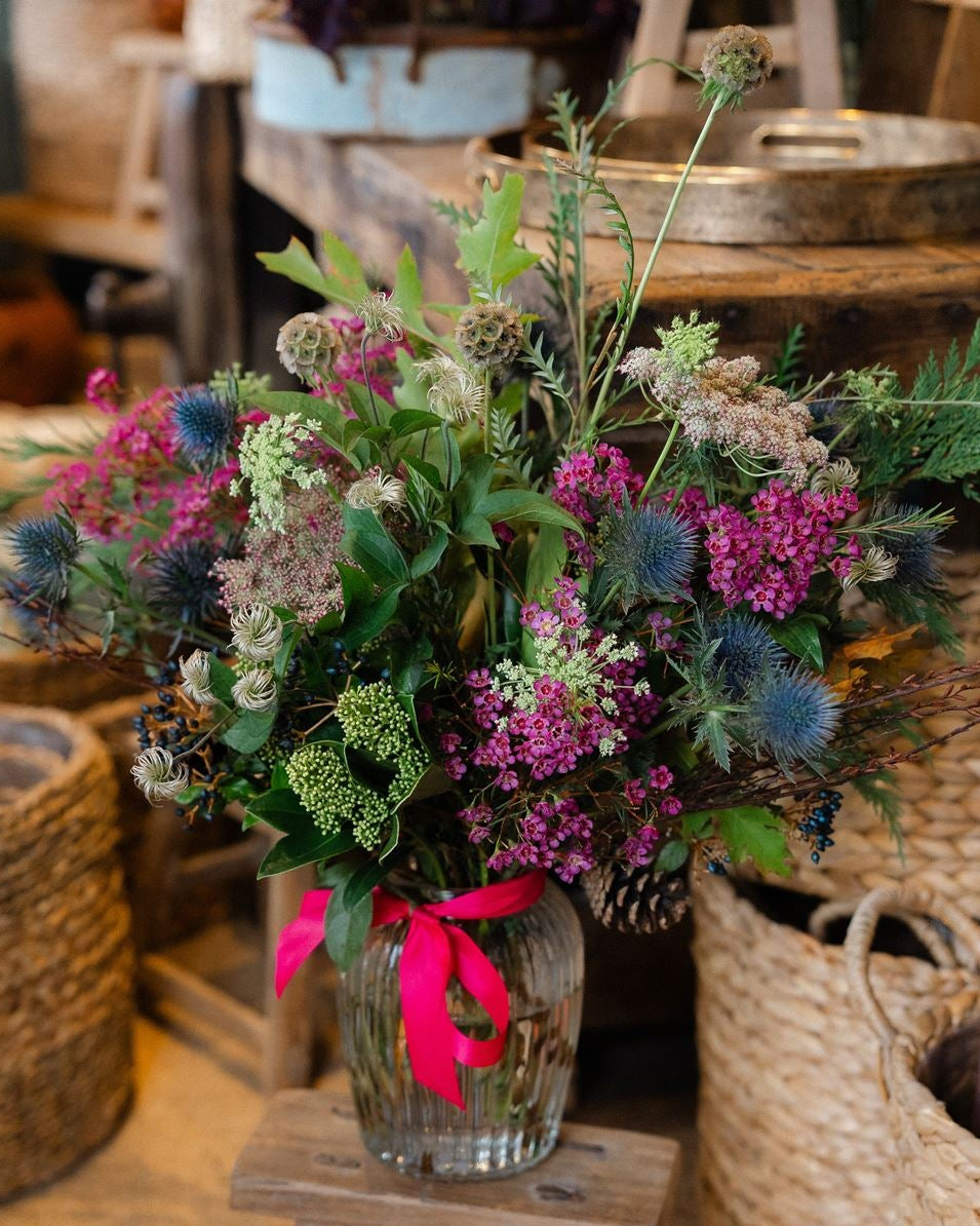 The Wild Revelry, a luxury Christmas hedgerow vase with jewel-toned flowers, thistles and sculptural seedheads. Handcrafted by Mad Lilies in Surrey.