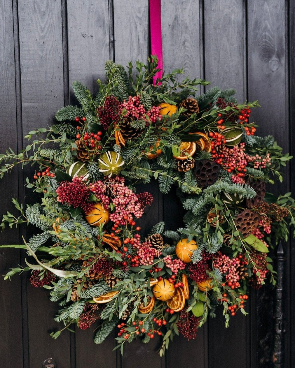 The Winterberry luxury fresh Christmas door wreath with pine, eucalyptus, red skimmia, rosehips, pink pepperberries, pinecones, dried oranges and limes.