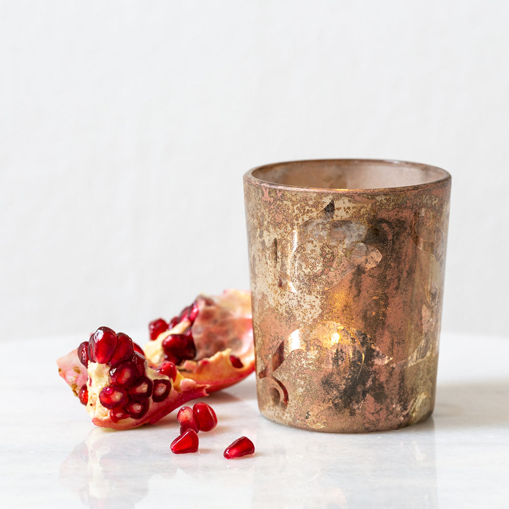 A gold-colored metal votive holder with an autumn leaf imprint
