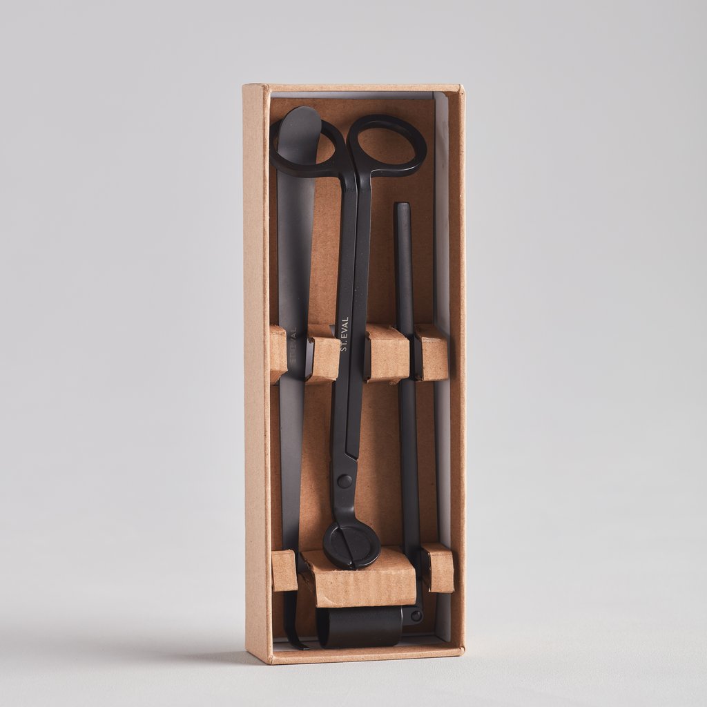 A set of matte black candle accessories within a wooden box, including a wick trimmer, dipper, and snuffer.