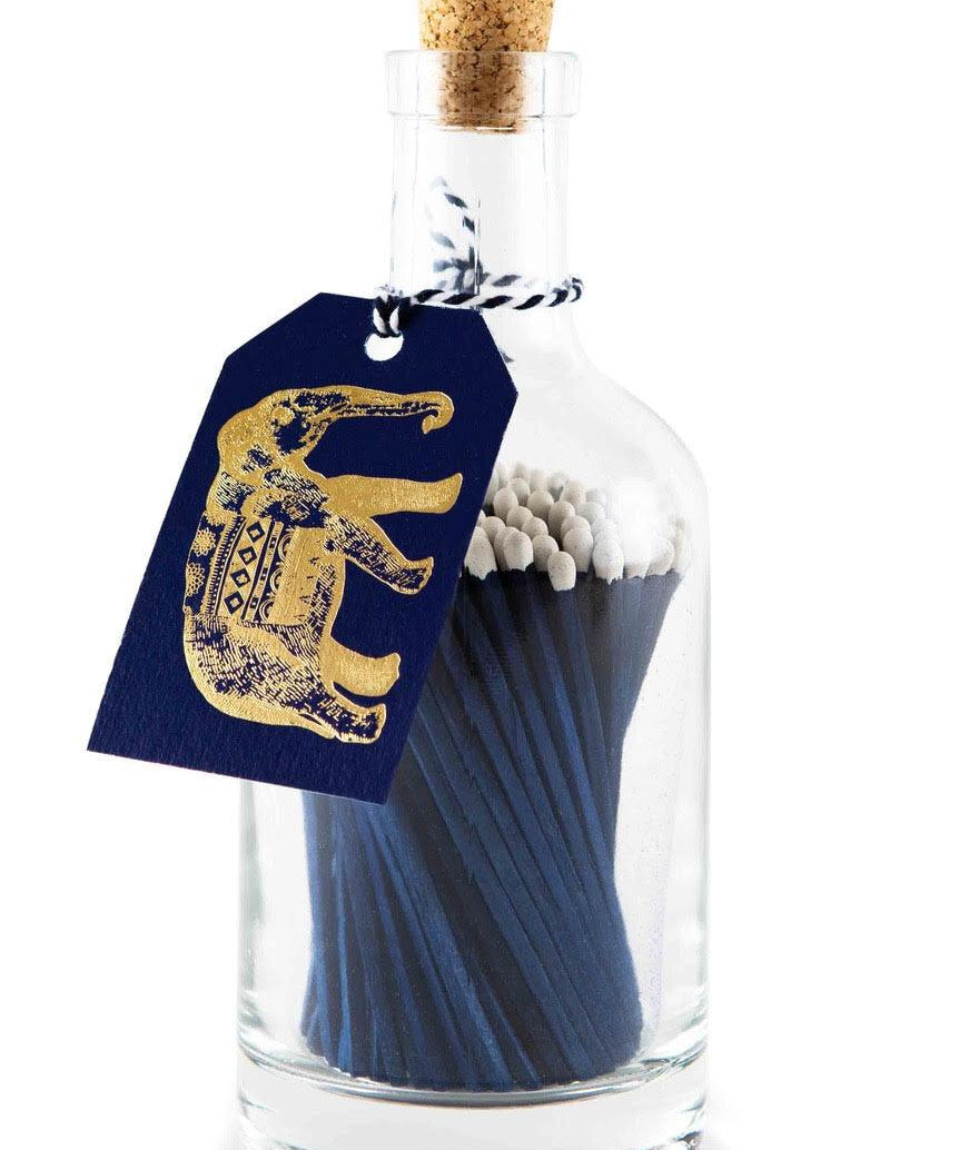 Archivist blue extra-long safety matches with white tips in a reusable glass bottle featuring a letterpress-foiled elephant label and cork stopper.