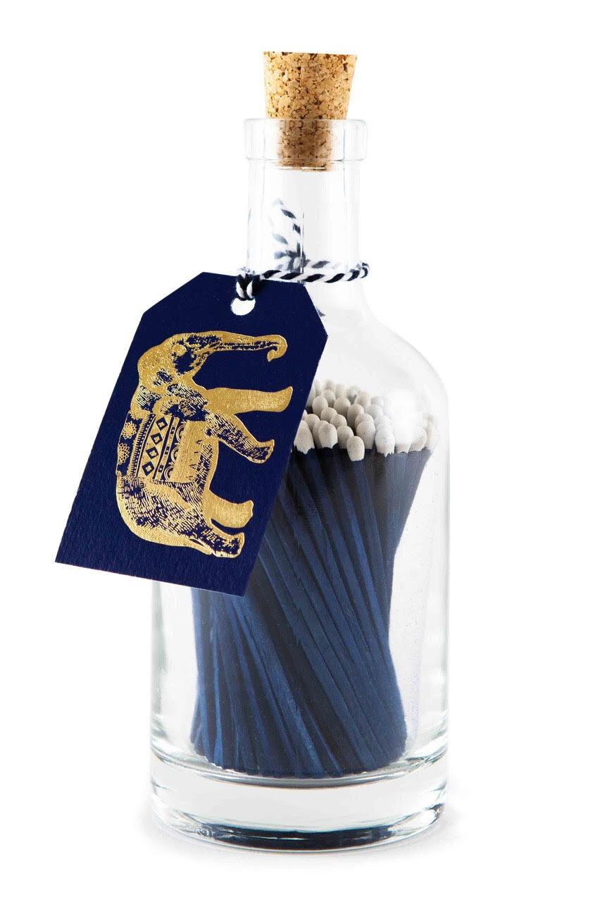 Archivist blue extra-long safety matches with white tips in a reusable glass bottle featuring a letterpress-foiled elephant label and cork stopper.